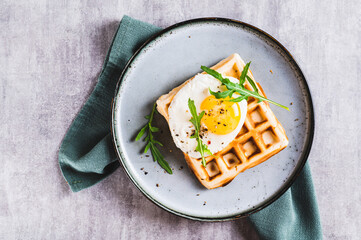 Close up of belgian waffle with fried egg, arugula and spices on a plate on the table top view