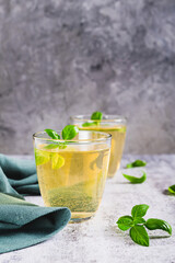 Organic basil lemonade in glasses and leaves on table vertical view
