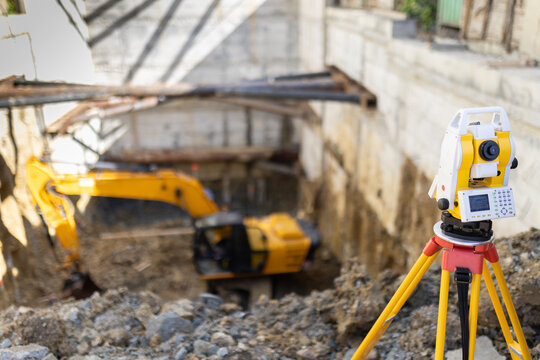 Construction site with surveying equipment and excavator working on foundation in urban area during bright daylight