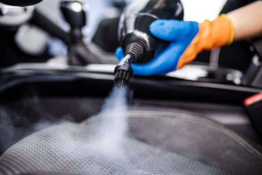 Cleaning the interior of a car with a steam cleaner during a detailed vehicle maintenance session at an auto detailing shop
