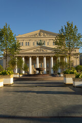Obraz premium The facade of the old building of the Bolshoi Theatre. Fountain in front of the building. Trees in tubs. Paved road. Bolshoi is the most famous theatre in Russia.