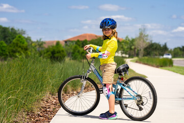 Naklejka premium Little kid boy ride a bicycle in the park. Kid cycling on bicycle. Happy smiling child in helmet riding a bike. Boy start to ride a bicycle. Sporty kid bike riding on bikeway. Kids bicycle.