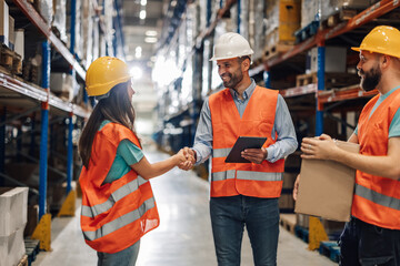 Warehouse workers shaking hands while holding digital tablet