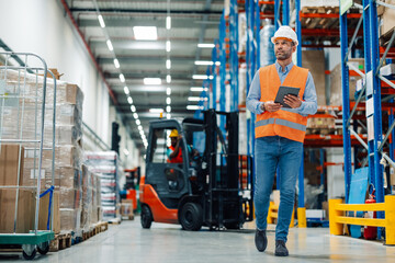 Warehouse manager walking and using digital tablet for managing goods and supplies