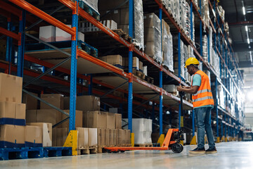 Warehouse worker moving pallet jack along aisle of shelves full of boxes