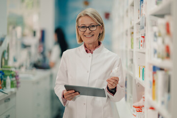 Senior pharmacist holding medicine and using digital tablet in pharmacy