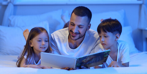 Happy father and children reading bedtime story in evening