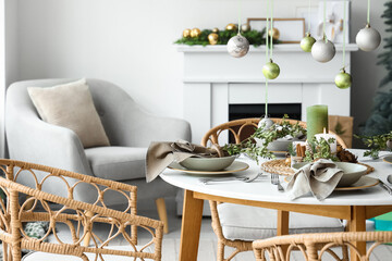 Christmas table setting with hanging balls, burning candles and pine cones in living room