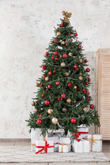 Decorated Christmas tree with gift boxes near white wall