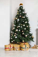 Christmas tree with gift boxes, silver baubles and Santa hat near white wall
