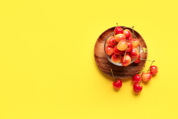 Glass cup with sweet cherries on yellow background