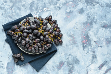 Plate with sweet black grapes on blue background