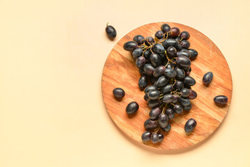 Wooden board with sweet black grapes on yellow background
