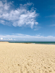 golden sunny sand beach with turquoise sea and white waves on a summer day with blue sky and fluffy clouds