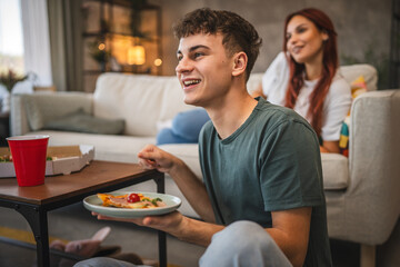 Young adult man sit on floor and eat pizza and watch movie at home
