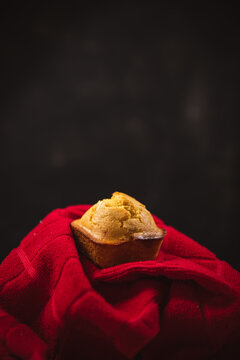 A cornbread muffin in a red towel against a black background