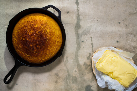 Corn cake cooked in a cast iron skillet on a table with a rustic plate of homemade butter