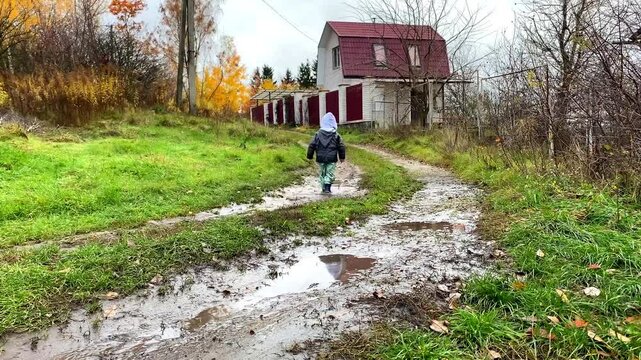 Little toddler child kid boy playing outside in boots in muddy puddle after rain in garden,home backyard at autumn.Carefree childhood.Moody fall weather forecast