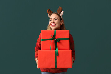 Beautiful young woman in reindeer horns with Christmas gift boxes on green background