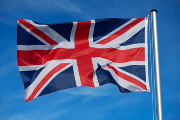 The flag of  Great Britain, United Kingdom, UK, flutters in the wind against a blue cloudless sky