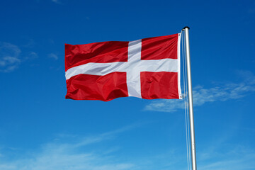 The flag of Denmark flutters in the wind against a blue cloudless sky