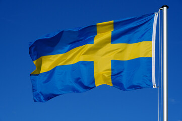 The flag of Sweden flutters in the wind against a blue cloudless sky