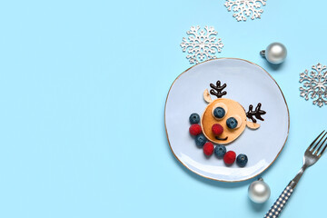 Plate with pancake in shape of reindeer on blue background. Christmas celebration