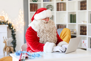 Santa Claus working with laptop at home on Christmas eve