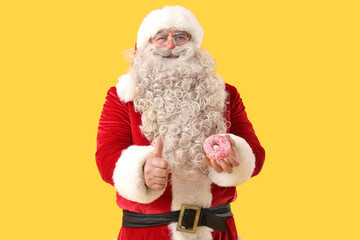 Santa Claus with tasty donut showing thumb-up on yellow background