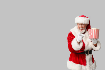 Santa Claus with bucket of tasty popcorn on grey background