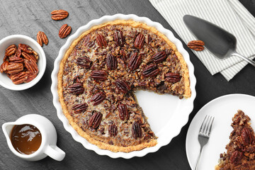 Delicious pecan pie, fresh nuts, caramel sauce and cake server on dark gray textured table, top view