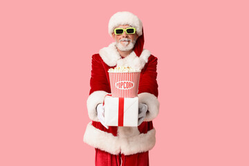 Santa Claus in 3D glasses with bucket of tasty popcorn and gift box on pink background