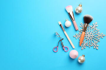 Makeup brushes, eyelash curler and Christmas decor on light blue background, flat lay. Space for text