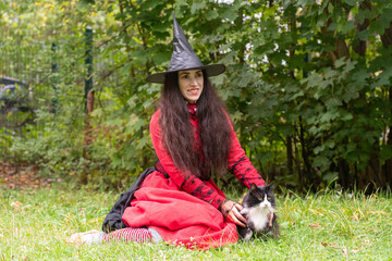 halloween, day of the dead holiday, dressed up witch with cat, black and white cat, pet in nature, cat on a leash, funny witch, fooling around at a party, black cap, red dress