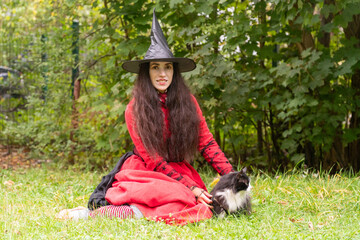 halloween, day of the dead holiday, dressed up witch with cat, black and white cat, pet in nature, cat on a leash, funny witch, fooling around at a party, black cap, red dress