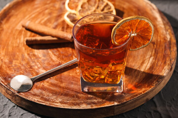 Wooden board with glass of delicious Old Fashioned Cocktail and orange slices on black grunge background