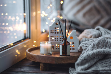 Aroma diffuser, burning candle, Christmas perfume on wooden bamboo tray, knitted sweater. Cozy home decor, hygge and aromatherapy concept. Comfortable atmosphere, Scandinavian decor. 