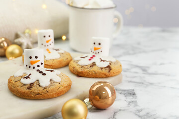 Delicious cookies with snowmen made of marshmallows on white table, closeup