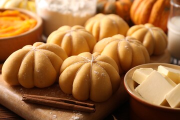 Raw pumpkin shaped buns and ingredients on wooden table, closeup