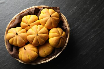 Wicker basket with tasty pumpkin shaped buns on dark textured table, top view. Space for text