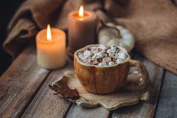 Spicy sweet fall hot drink: delicious pumpkin latte with cinnamon, marshmallow with salted caramel. Served in handmade artisan mug in shape of pumpkins, cozy home decor with candles, dry autumn leaves