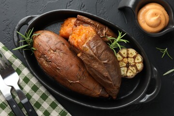 Tasty cooked sweet potatoes served with rosemary and sauce on black table, top view