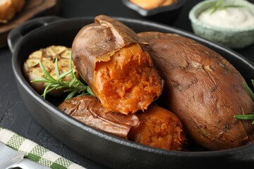 Tasty cooked sweet potatoes, rosemary and garlic on black table, closeup