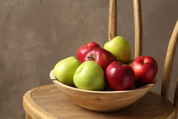 Ripe red and green apples in bowl on wooden chair near grey wall