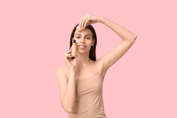 Beautiful young woman applying foundation by makeup sponge on pink background