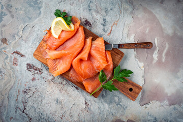 Traditional Norwegian smoked salmon in slices with parsley and lemon served as top view on a rustic wooden chopping board with text space © HLPhoto