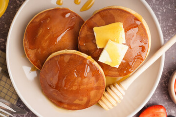 Tasty pancakes with honey and butter on table with berries on grey background