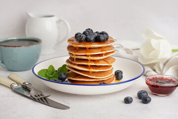 Plate with tasty pancakes, cup of tea and cutlery on white table