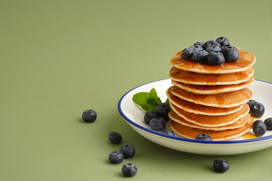 Plate with tasty pancakes and blueberries on green background