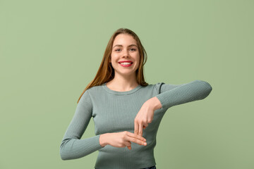 Young deaf mute woman using sign language on green background